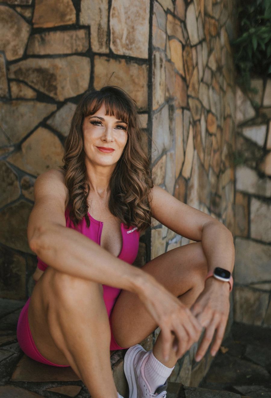 A UNLMTD woman in a pink set sitting by a stone wall